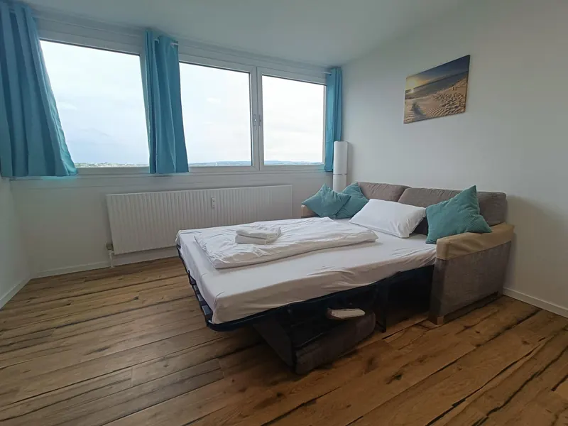 Ausgezogenes Schlafsofa vor einem Fenster mit blauen Vorhängen